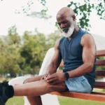 Older man holding his painful knee while resting on a park bench, a common sign of knee osteoarthritis